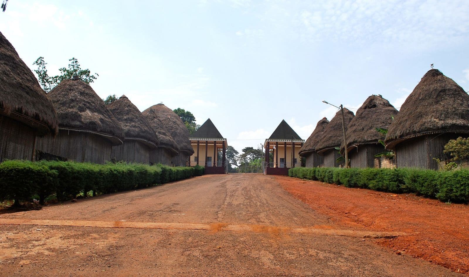 Allée de terre rouge bordée des cases à toit de chaume d'une chefferie bamiléké, près de Bafoussam